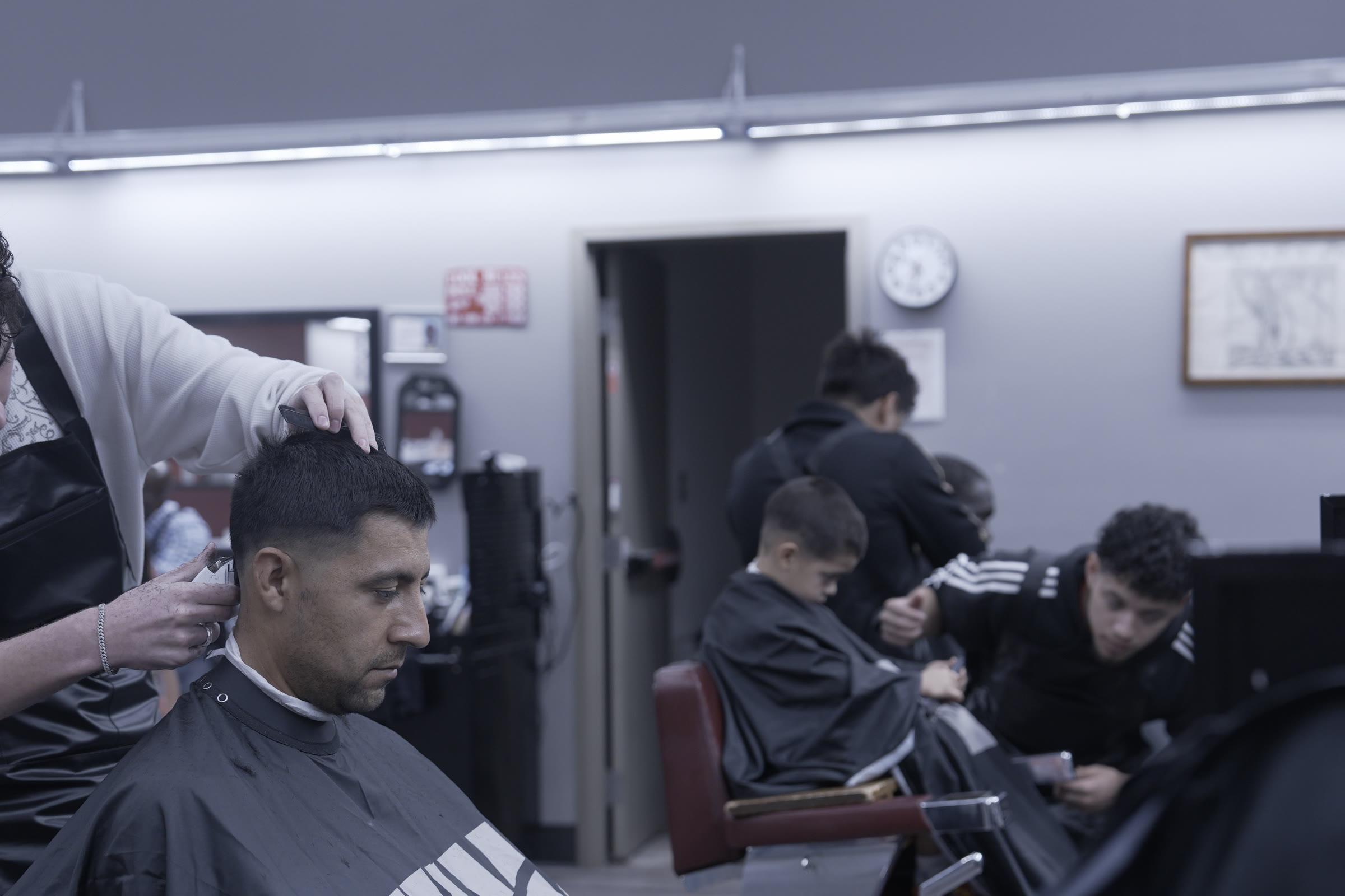 A student cutting a client's hair at a station, with two more students working at the chairs behind them.