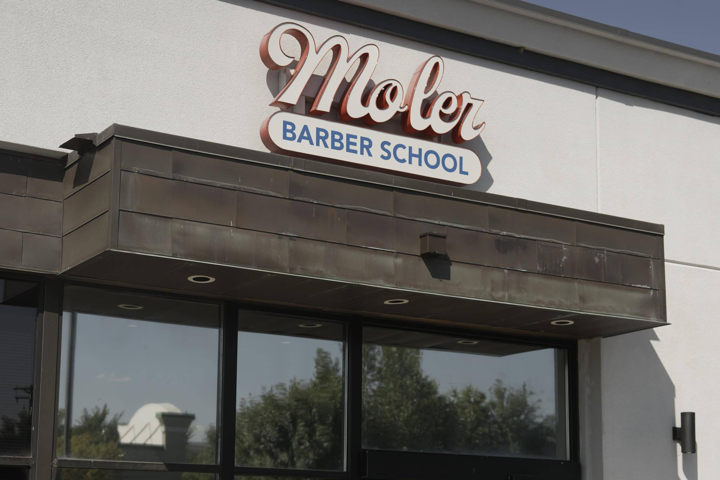 The Moler Barber School sign in red script above the entrance on 53rd Ave NE in Fridley, seen from the parking lot.