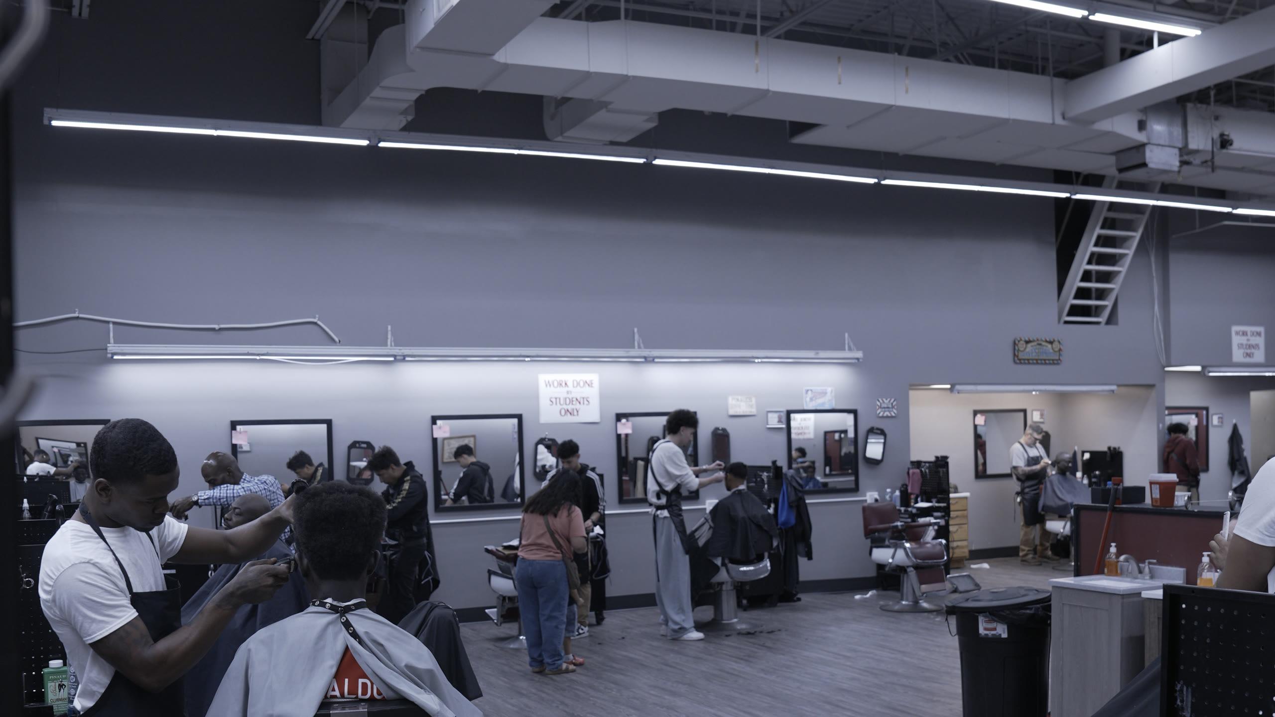 The student floor at The Original Moler Barber School, a row of mirrored stations with students cutting and most of the chairs occupied.