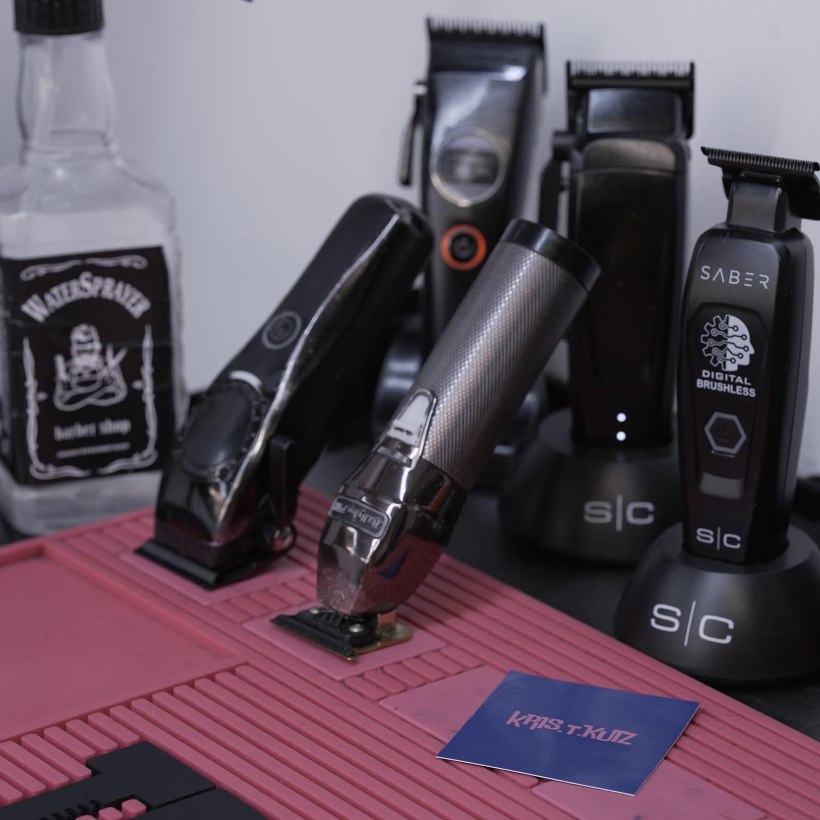 A student's station, clippers and trimmers upright on their charging stands beside a water sprayer and a comb mat.